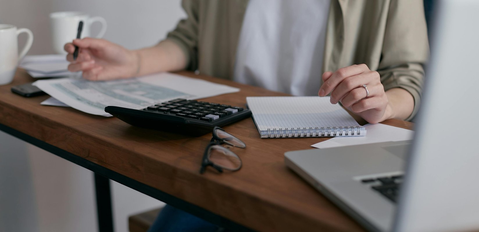 A person holding a pen over financial papers next to a laptop and a calculator